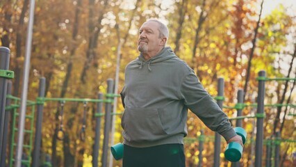 An elderly man is lifting dumbbells in a park - Powered by Adobe