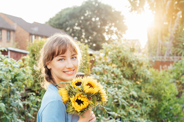 Portrait of smiling tender young woman holding fresh sunflowers bouquet and enjoying carefree...
