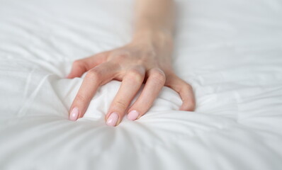 Obraz na płótnie Canvas A woman's hand is squeezing a white blanket on the bed, close-up. Pain during sleep, a dangerous health condition