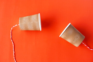 DIY paper cups with string on red background. Concept, telephone toy. Concept, telephone toys which...
