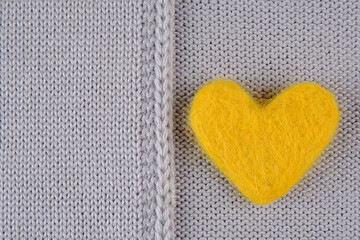 A yellow heart made of wool lies on a gray knitted background.The concept of handmade, needlework, hobbies, sale of yarn for knitting.A cozy background for greeting cards for the winter holiday.