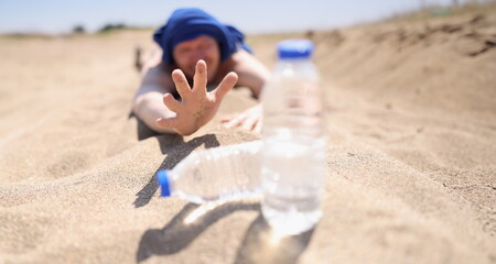 A man lies on the sand reaching for a bottle of water, close-up, blurry. Extraordinary event,...