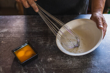 Baker's hands beating eggs with a hand mixer on a white plate, separating the yolks from the whites. Cooking in the traditional way