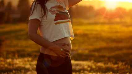 Pregnant woman at sunset happy with hands on belly in first weeks of happy pregnancy in nature
