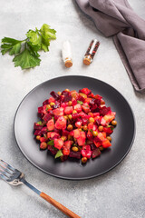 Vinaigrette with beetroot and boiled vegetables, traditional Russian homemade salad. A black plate on a light background.