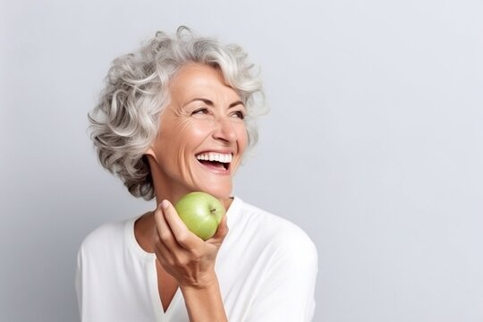 Beautiful cheerful smiling mature woman bites a green apple.
