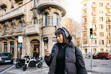 Fototapeta na wymiar Young woman walking with wireless headphones and using a phone while walking on a city.