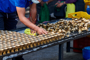 Nepali temple staff pour out candle oil after wick burns out for replacement, cleaning bronze candle holders reuse, volunteer work in for Boudhanath Stupa temple in Kathmandu - obrazy, fototapety, plakaty