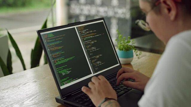 Transgender developer programs in coworking space. Inclusive tech pro codes on laptop, focused, efficient. Plant beside, diverse workspace vibe. Video illustrates modern programming, representation.