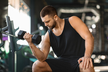 Fototapeta na wymiar Bearded Male Athlete Making Seated Biceps Curl Exercise At Gym