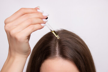 A young woman applies a drop of oil from a pipette to her scalp, close-up. Vitamins, keratin for...