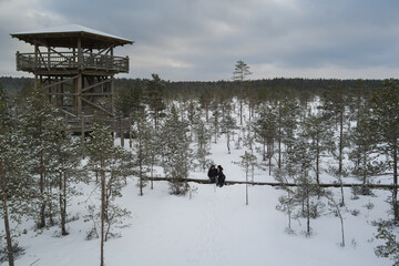 A young couple of travelers rests in winter outdoors in the forest near the observation tower on...