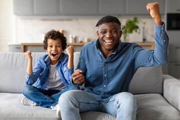 Joyful black father and son celebrating victory at home