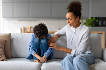 Concerned black mother comforting her sad child son at home