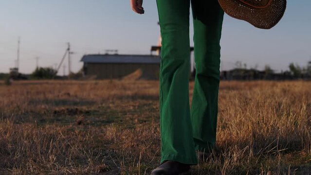 Man in green bell-bottom jeans and leather boots walks forward towards the camera across a field of dry grass.