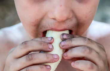 A peeled banana is eaten by a poor little boy with dirty hands and a dirty face.