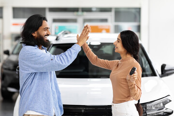 Young indian man and woman giving high five, buying car
