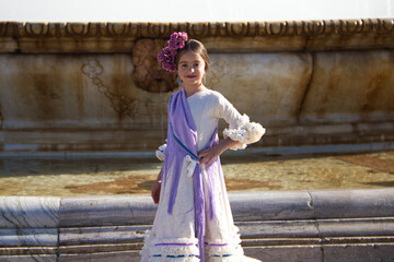 a pretty little girl dancing flamenco dressed in a beige dress with ruffles and purple fringes in a...