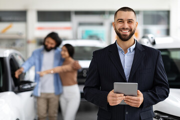 Handsome young salesman with digital tablet in luxury dealership salon