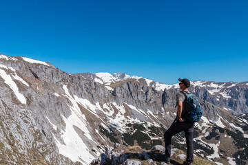 Hiker man with panoramic view of majestic mountain peak Ringkamp in wild Hochschwab massif, Styria, Austria. Scenic hiking trail in remote Austrian Alps on sunny day. Wanderlust in alpine spring