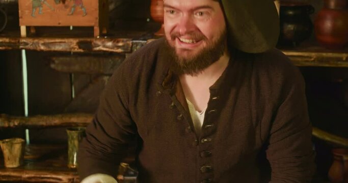 Bearded seller seeks purse with money in store. Complaisant merchant pays tax from profit to collector in medieval tavern. Smiling man trades in shop