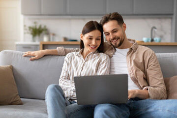 Couple smiling and using laptop computer on couch at home