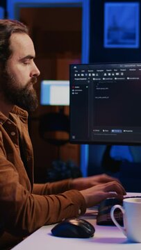 Developer overthinking solutions while doing programming during remote job shift in home office. IT admin working on computer in apartment late at night, thinking how to fix bugs, camera B