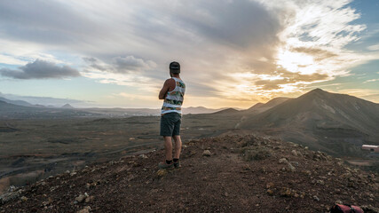 A man admires the view from the top of the mountain at the sunset after climbing a crater and...