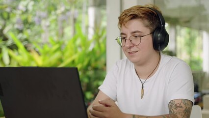 Transgender individual in a coworking space participates in a virtual meeting, engaging with participants and contributing ideas, showcasing remote collaboration amid a light-filled, modern workplace.