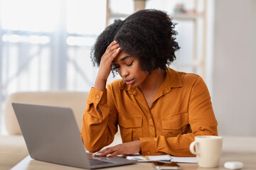 Stressed African American woman in a mustard blouse shows signs of frustration or headache