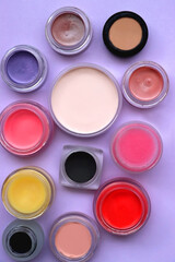 Bowls with various colorful cream beauty products on purple background. Top view.