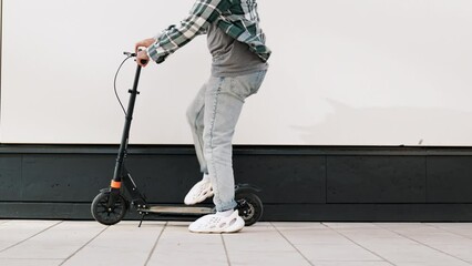 Trendy smiling bearded man in casual clothes riding electric scooter in urban background. Handsome model posing in the street. Hipster guy with curly hairstyle. Cheerful and happy. He comes and rides