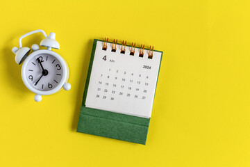 Desk calendar for April 2024 and clock for planning on a yellow background.