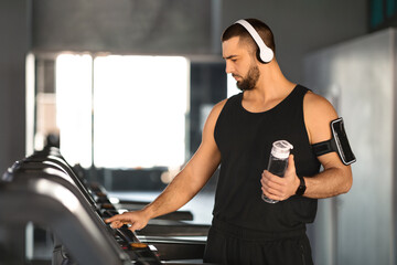 Fitness-focused man holding water bottle while operating treadmill at gym