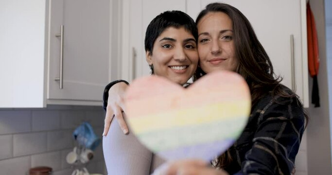 Happy girl friends lesbian couple embracing and holding a heart shaped rainbo