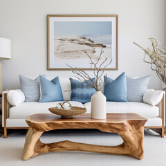 Live edge accent coffee table near white sofa with blue pillows against wall with big poster frame. Coastal home interior design of modern living room