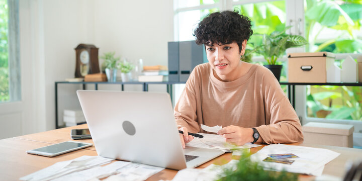 A Young Asian businesswoman is checking financial documents, calculating bills or taxes expense or payment at home, using laptop and calculator, investment or insurance planning, money saving control.