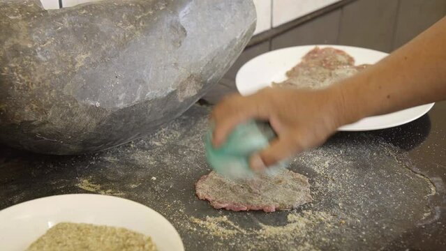 traditional Bolivian food called "silpancho". Cooking process, hand pounding a piece of meat seasoned with breadcrumbs and pepper on a traditional stone worktable called "Batan" Bolivian tradition.