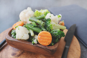 frozen vegetables. Wooden eco-friendly bowl with frozen vegetables on the table, green peas, carrots, cauliflower, green beans. Vegetable preservation concept.