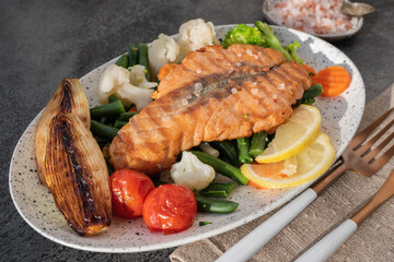 Grilled salmon steak with vegetables - cauliflower and broccoli, tomatoes and shallots. Healthy eating concept.