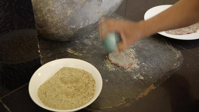 traditional Bolivian food called "silpancho". Cooking process, hand pounding a piece of meat seasoned with breadcrumbs and pepper on a traditional stone worktable called "Batan" Bolivian tradition.