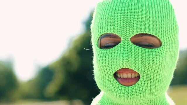 Closeup portrait of beautiful sexy smiling woman. Model wearing bandit balaclava mask. Hot seductive female  posing in street at sunny day. Crime and violence