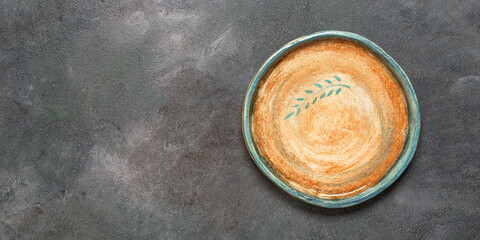 Empty handmade ceramic plate with a pattern on a dark grunge background. Top view, flat lay, copy space. Banner.