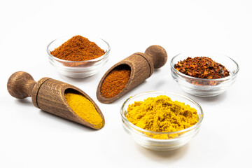 Spices in wooden spoons and glass bowls isolated on a white background in close-up.