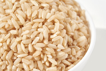 A bowl of uncooked brown rice, isolated against a white background. Healthy, savory dish includes...