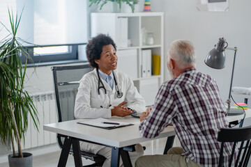 Doctor specialist consulting a patient in a doctor's office at a clinic. Female doctor is talking with a male elderly patient.