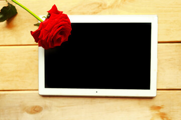 Black mockup tablet and red rose on wooden background. Valentines Day greeting card