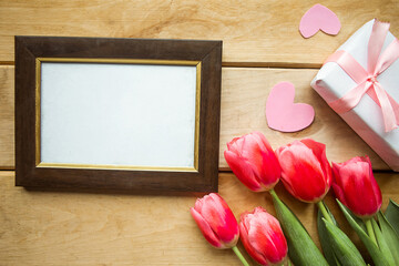 Pink tulips, mockup photo frame and gift box on wooden background. Flat lay, top view, copy space. Women's Day or Mother's Day greeting card