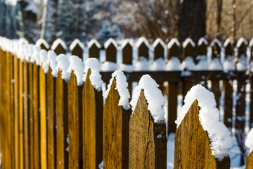 A fence made of pointed boards covered with a layer of snow on a winter day
