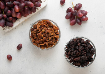 Two bowls with dried raisins with ripe red grapes on light background.Top view.